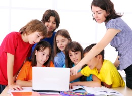 Teacher instructing elementary schoolchildren on using the laptop computer.